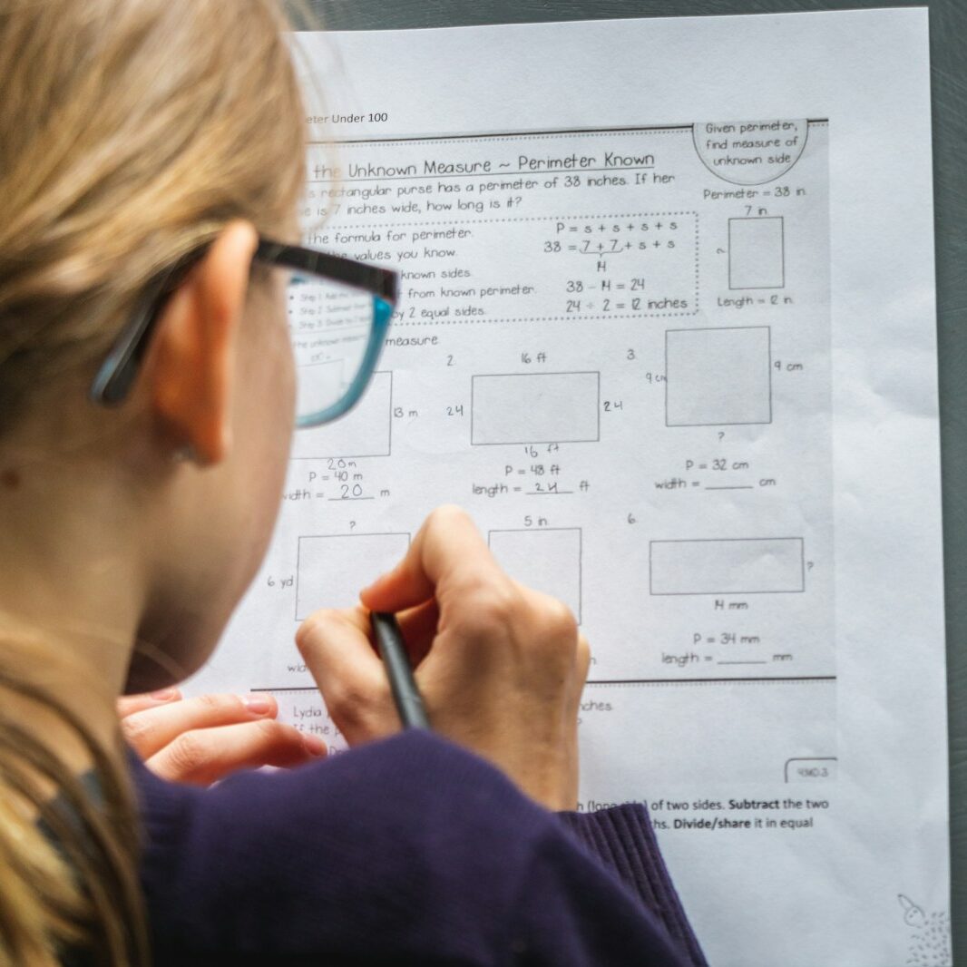 child in black framed eyeglasses completing math worksheet on geometry