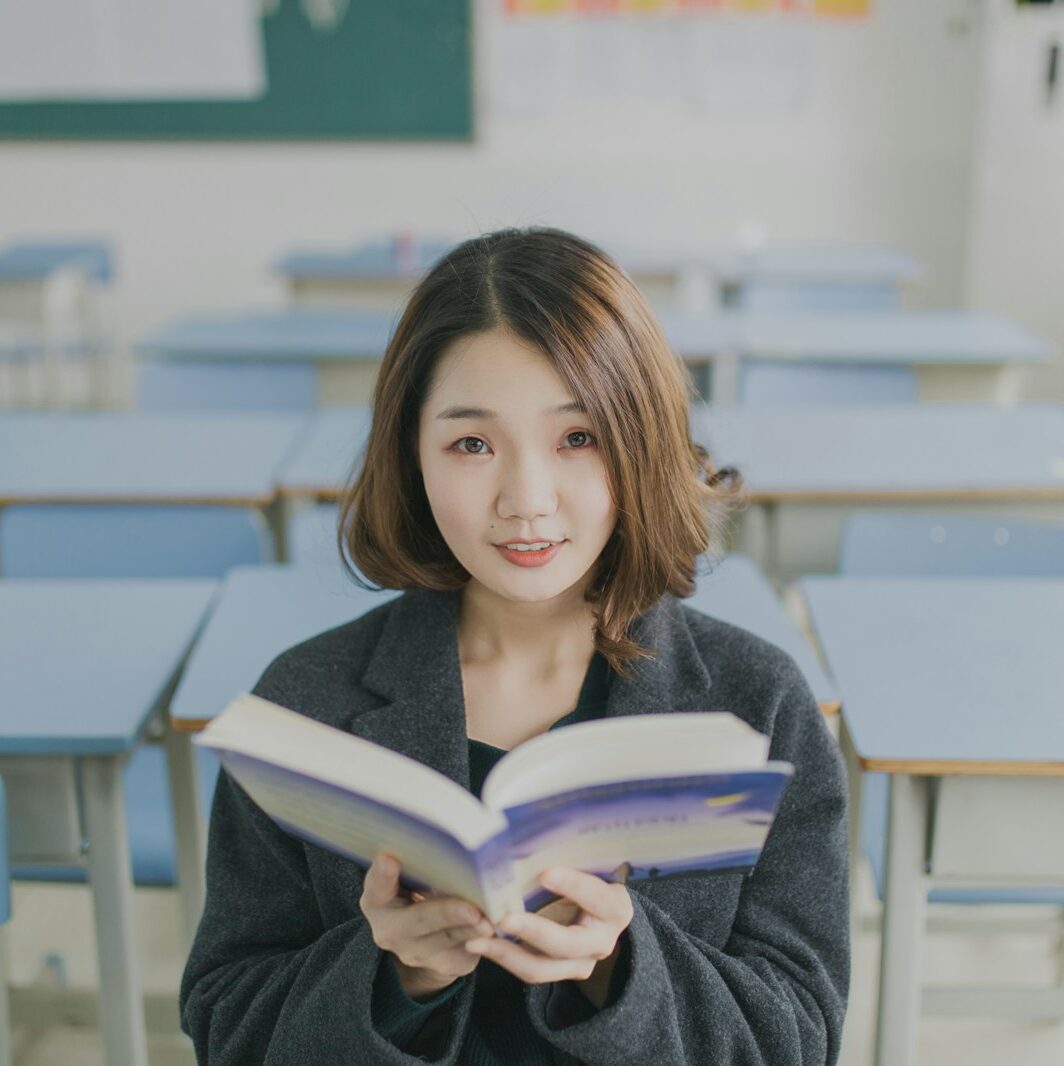 woman reading book sitting at desk in classroom